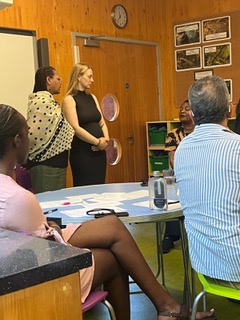 Facilitators standing and speaking with participants seated around a table during a workshop.